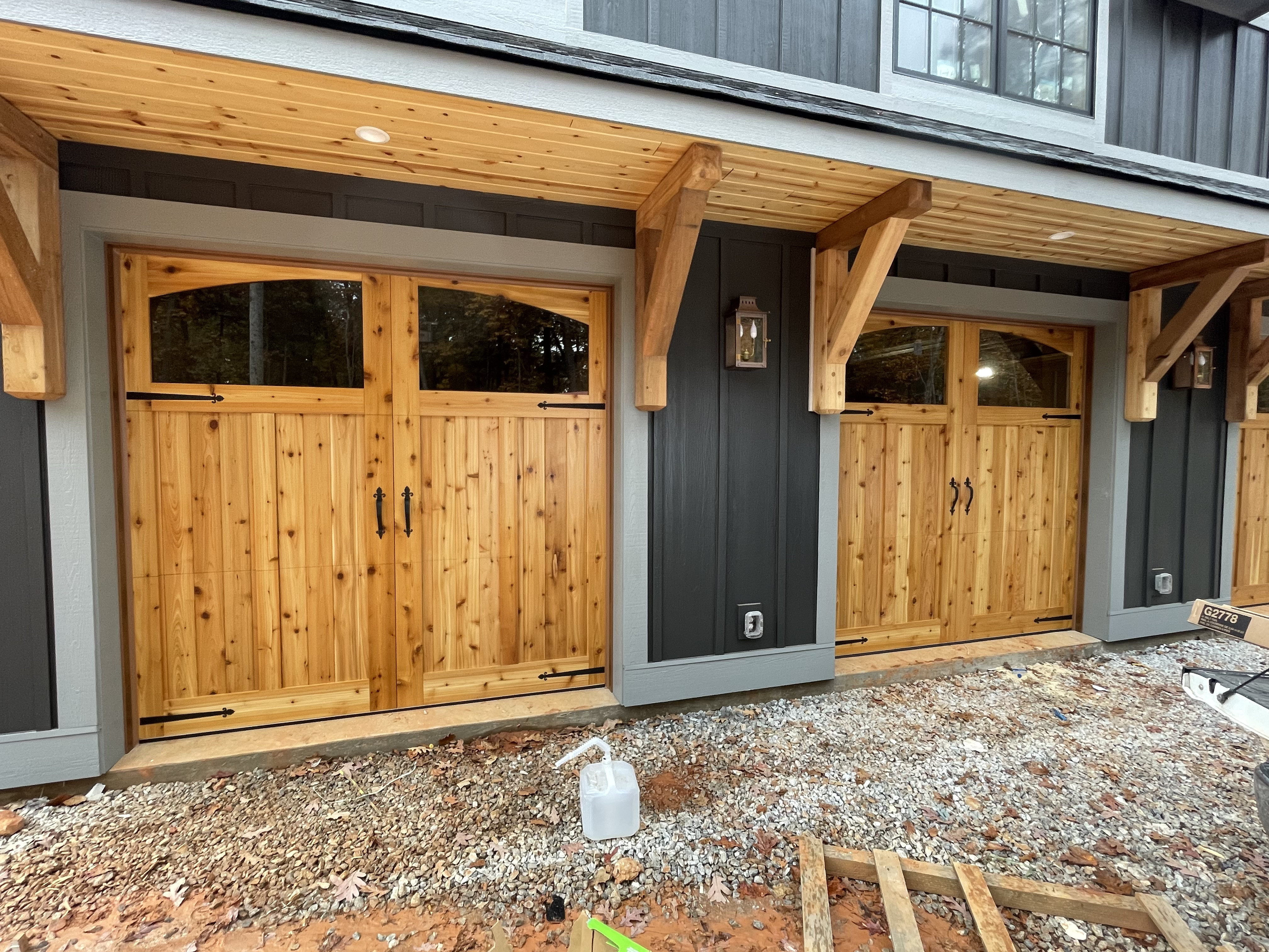 Handcrafted cedar barn doors with timber brackets on dark siding home by Old Wood Dynasty