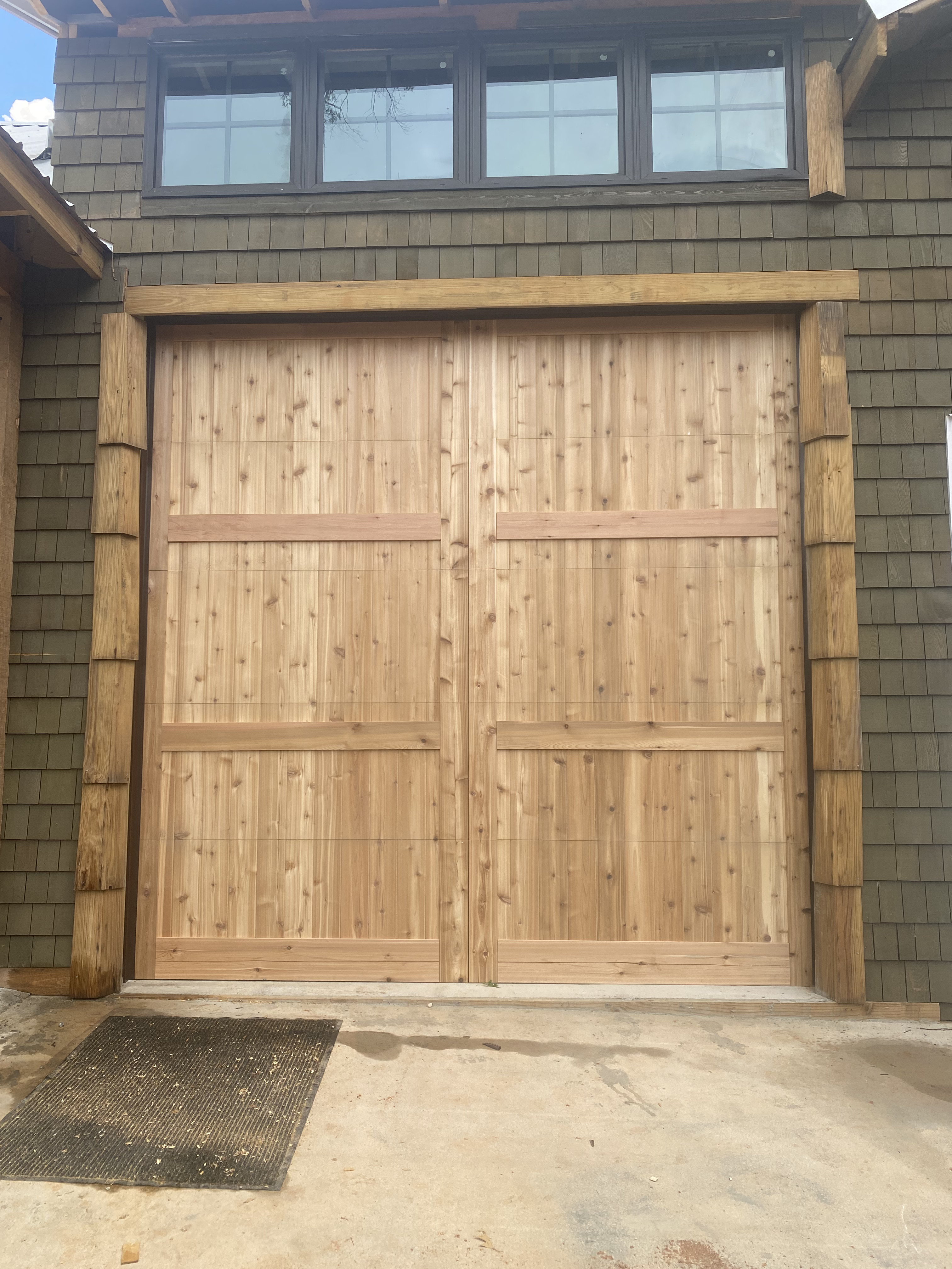 Handcrafted cedar flat panel garage door on green shingle siding home by Old Wood Dynasty