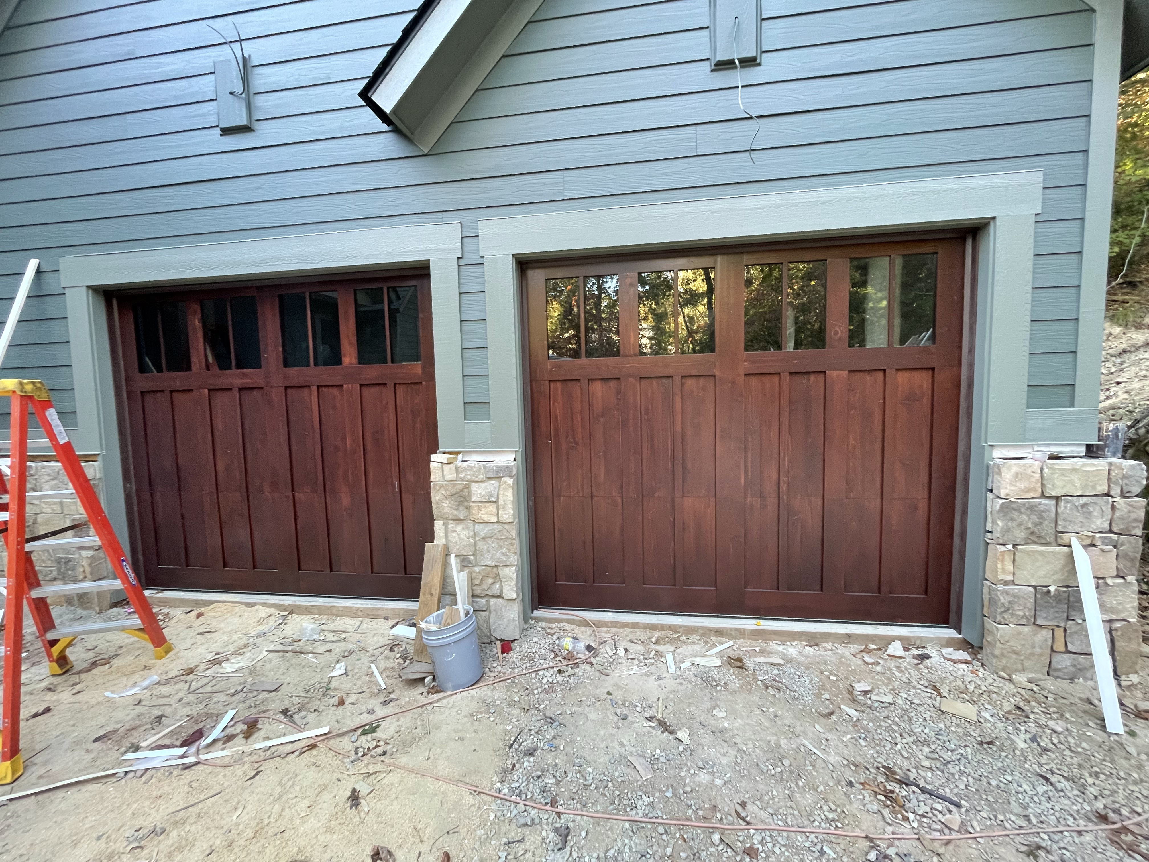 Custom dark stained wooden double garage doors with blue siding by Old Wood Dynasty