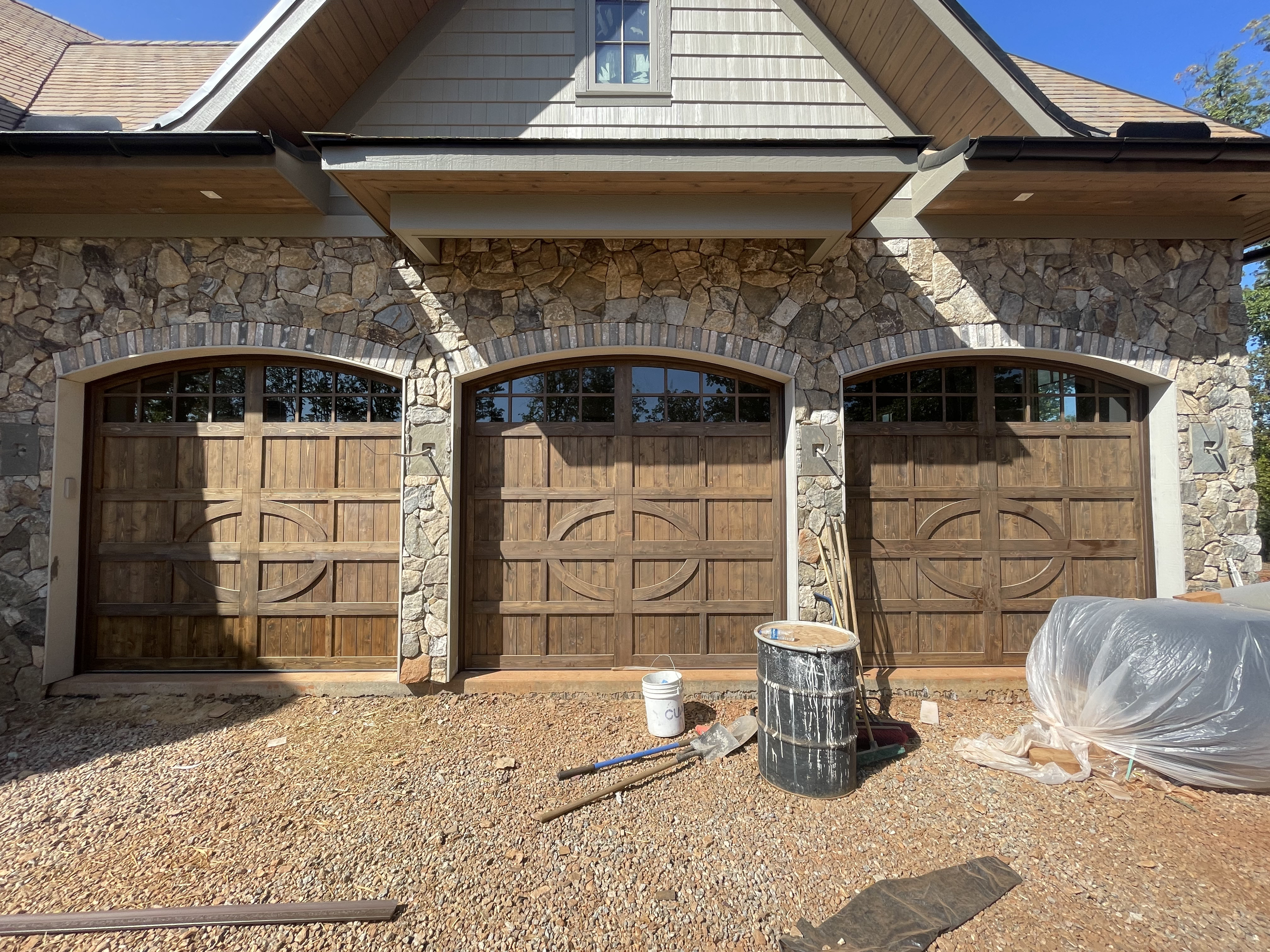 Custom ornate oval panel triple bay wooden garage doors on stone home by Old Wood Dynasty