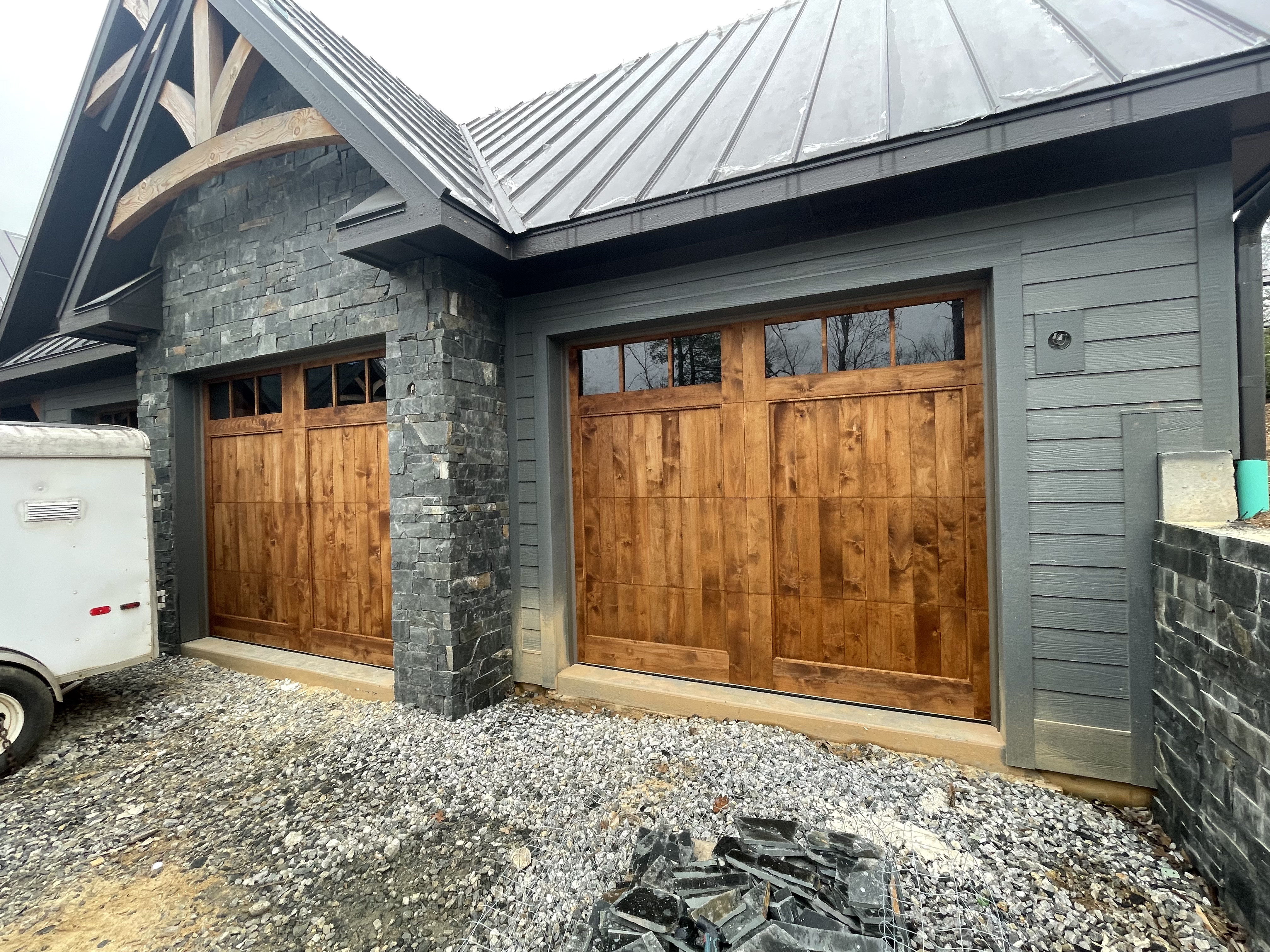 Custom rustic wood double garage doors with stone and gray siding by Old Wood Dynasty
