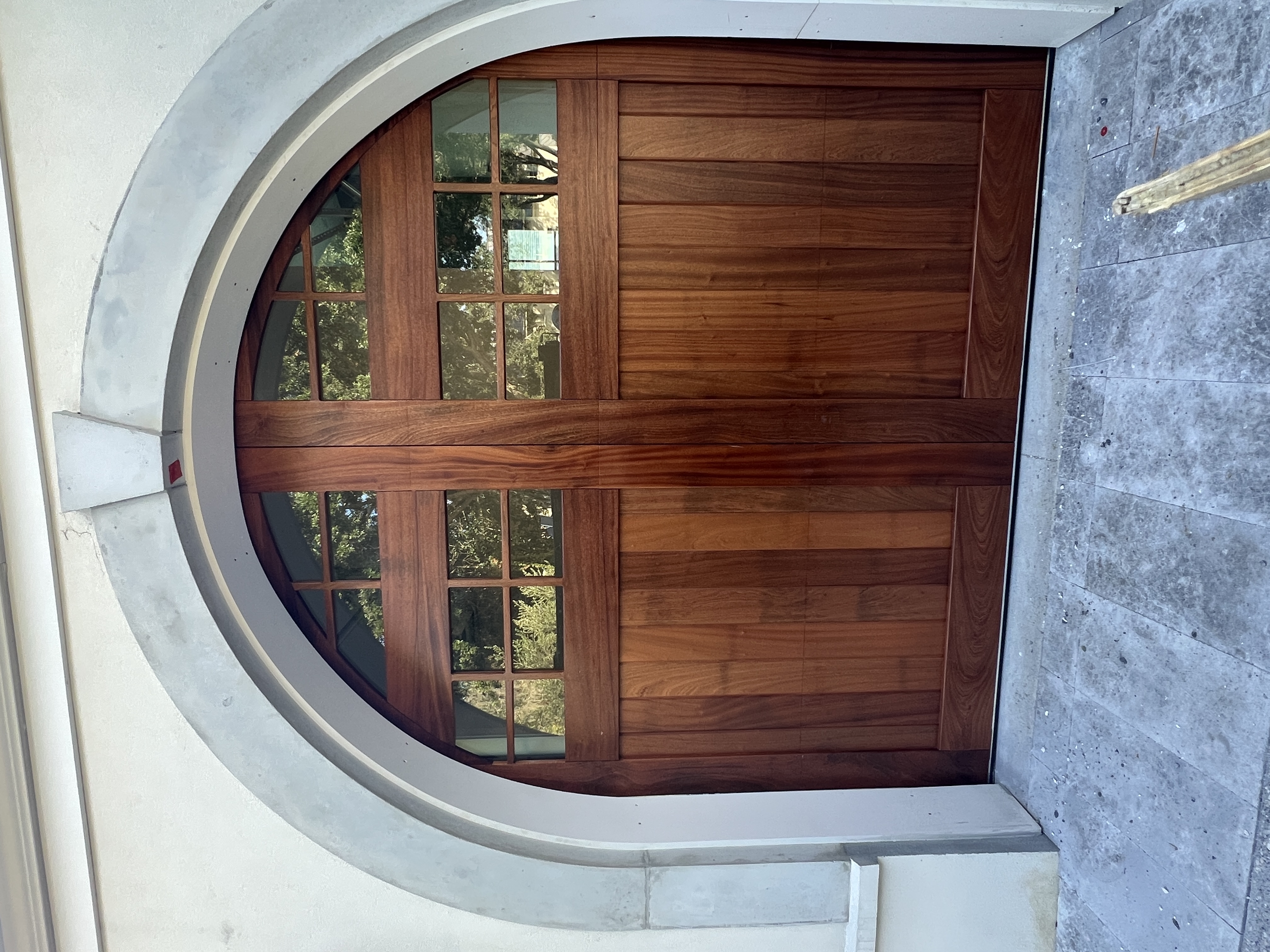 Custom sapele arched garage door with gridded windows and stone surround by Old Wood Dynasty