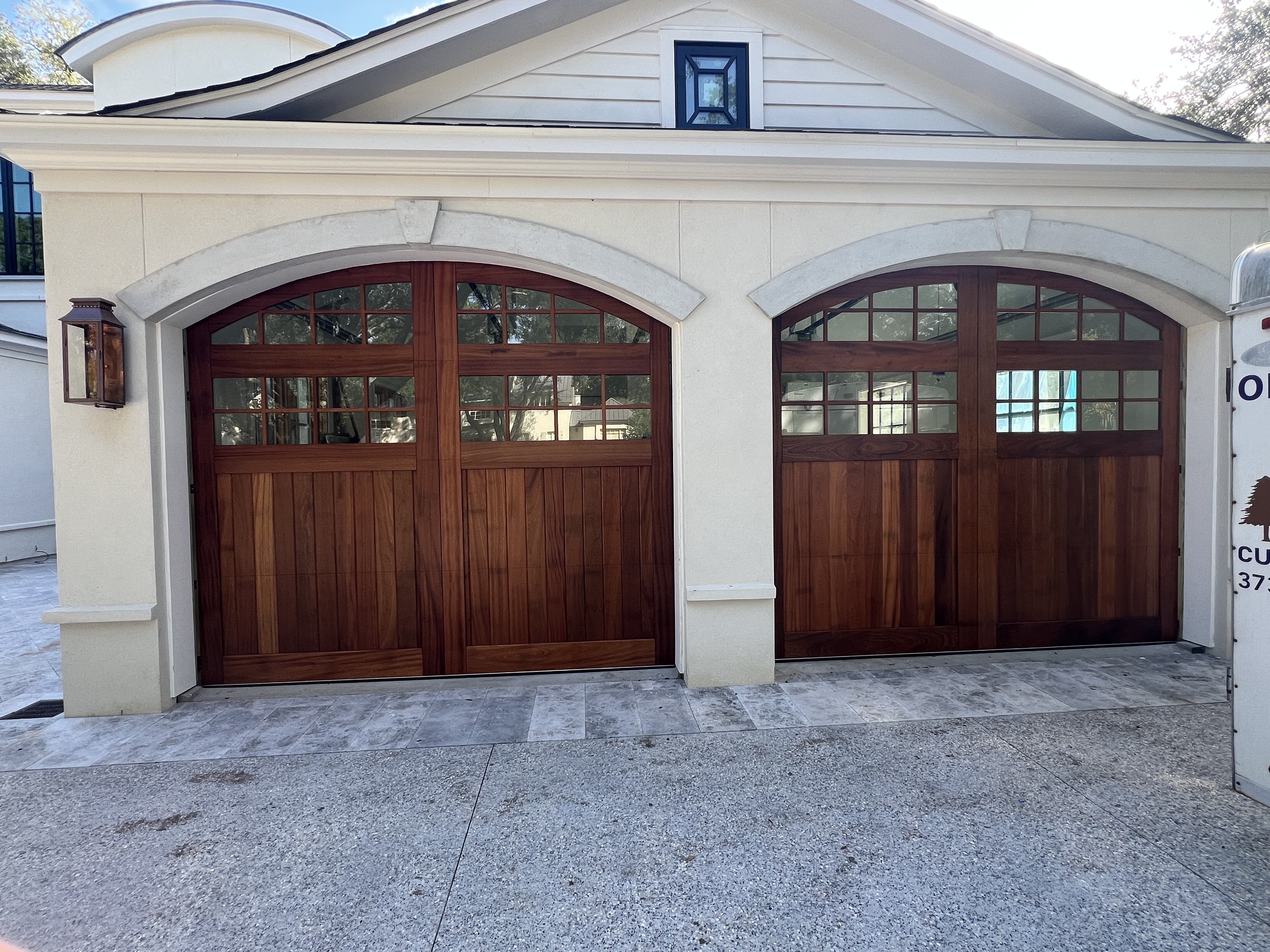 Custom sapele double arched wooden garage doors on stucco home by Old Wood Dynasty
