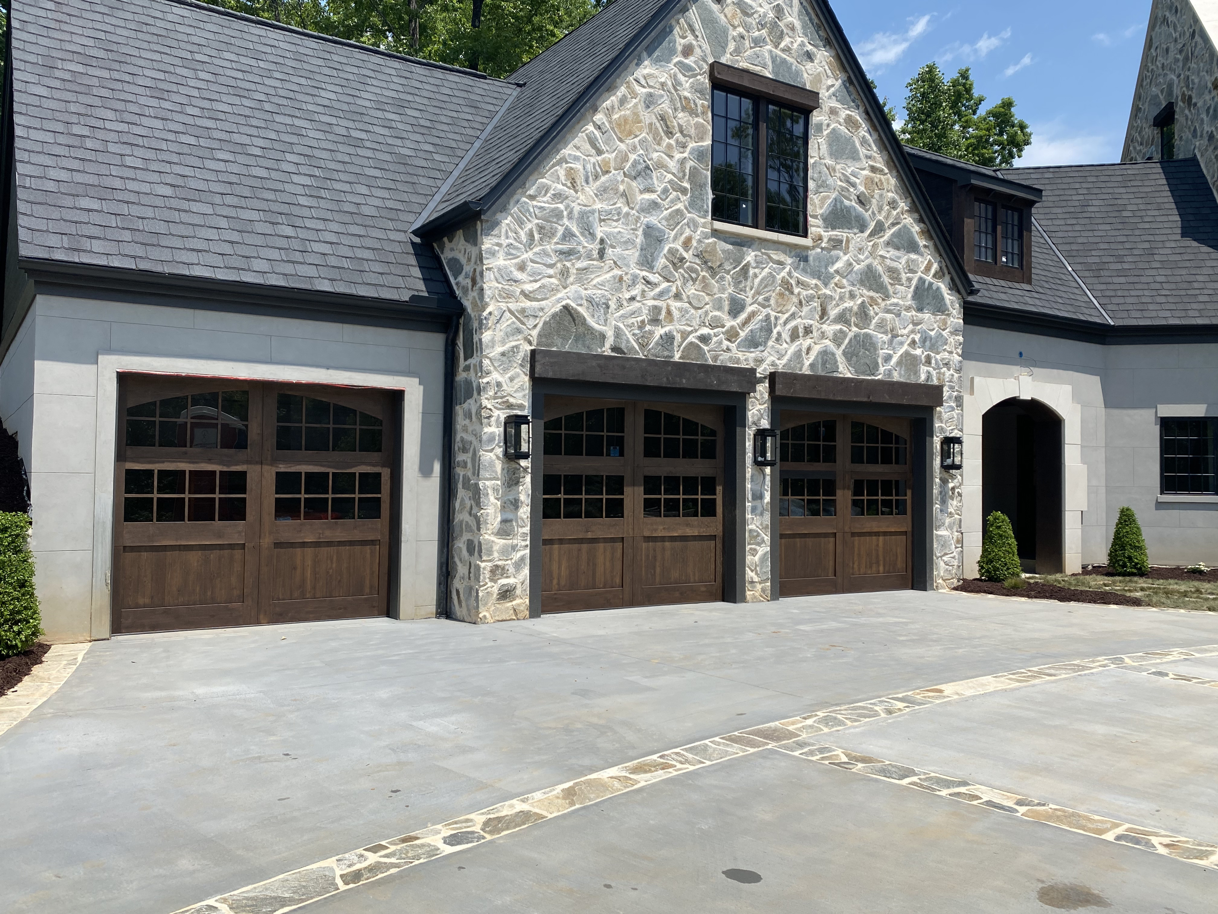 Three custom stained wood carriage-style garage doors on stone home by Old Wood Dynasty